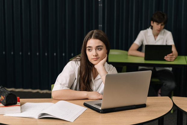 A young person sitting at a school desk using a laptop