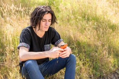 Young person sat in field on their phone